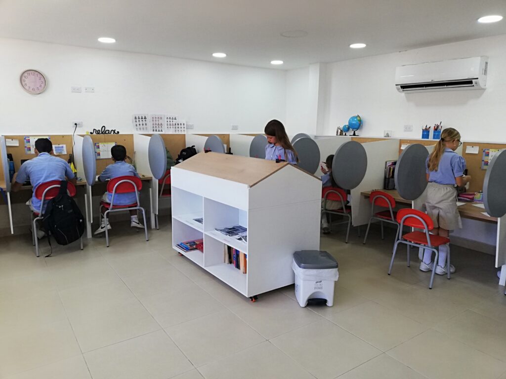 Dos estudiantes trabajan en la mesa central de la sala de estudio, con las oficinas individuales al fondo