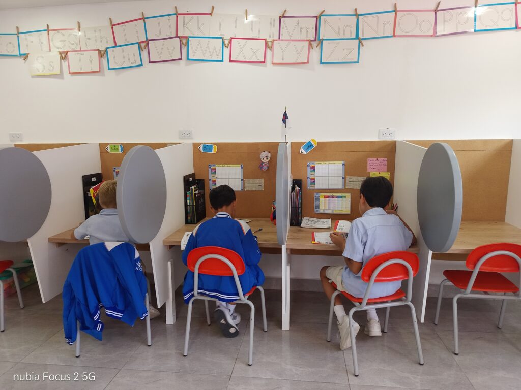 Una supervisora atiende desde su escritorio mientras los estudiantes trabajan en la sala